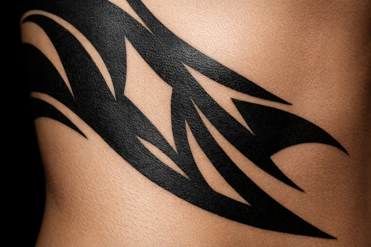 A bold black tribal tattoo wraps around a person's side against bare skin.