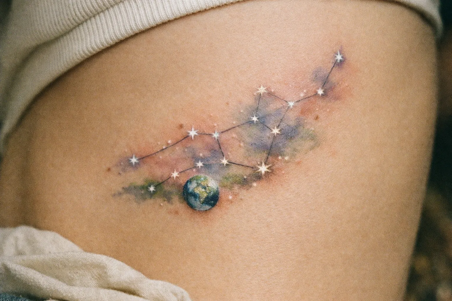 A Virgo constellation tattoo with the Earth and watercolor effects on a person's upper thigh.