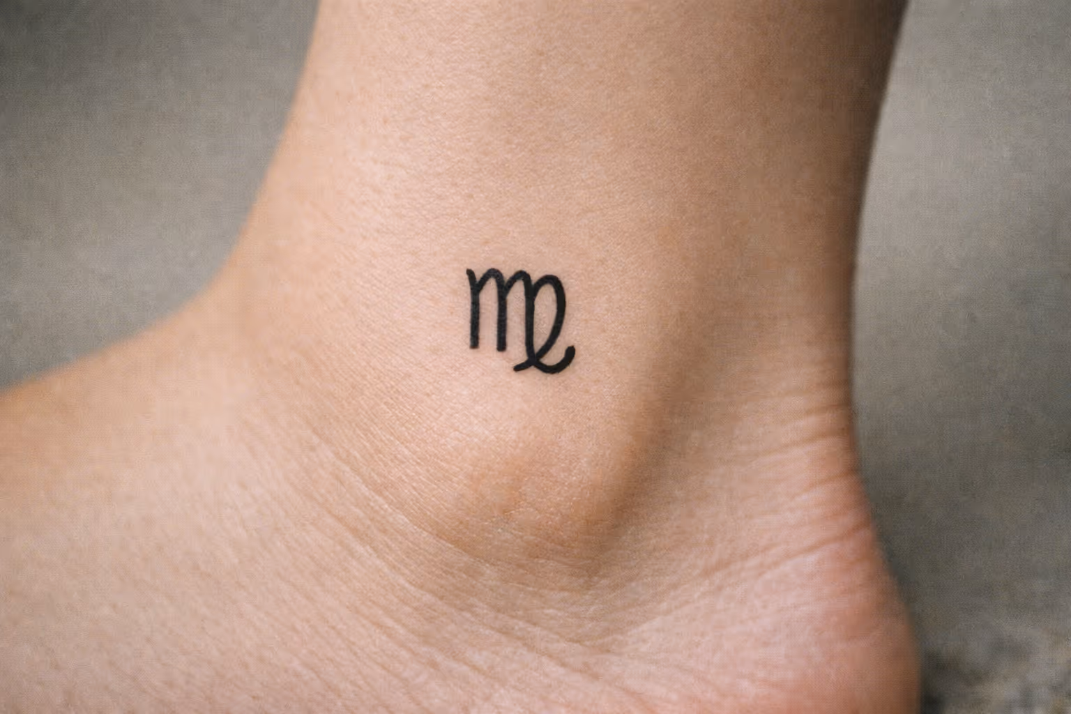 A small Virgo zodiac symbol tattooed on a person's ankle.