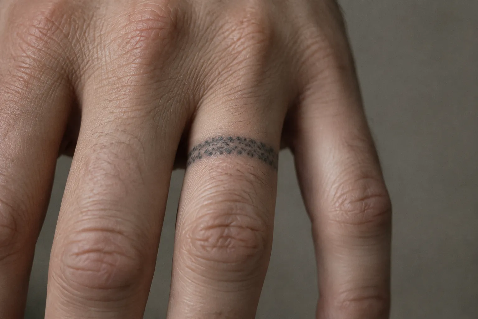 A close-up of a hand showing a faded dotted ring tattoo around a finger.
