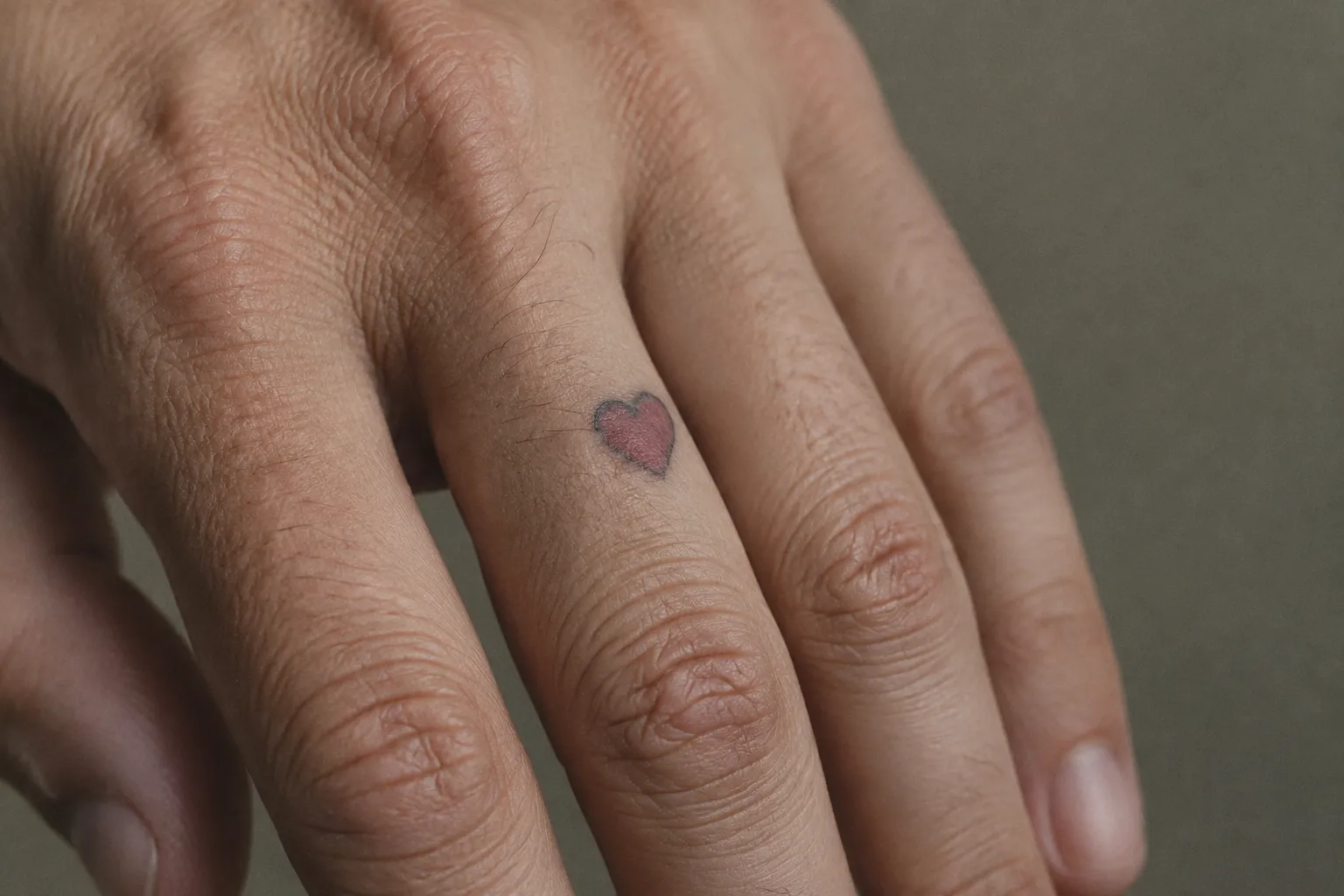 A hand with a small faded heart tattoo on a finger.
