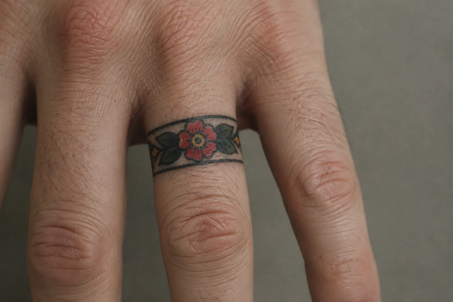 A hand with a colorful floral band tattoo around one finger.