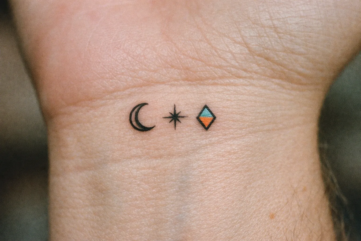 A small tattoo with a crescent moon, star, and geometric shape on the inner wrist.