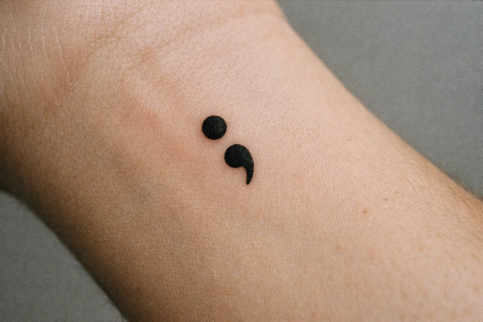 A semicolon tattoo on the inside of a person's wrist.